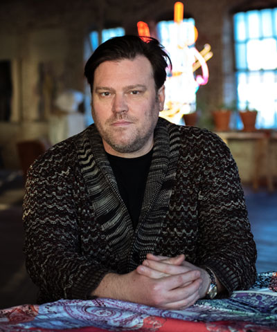 Portrait of the artist Elliott Hundley in a room with hands folded