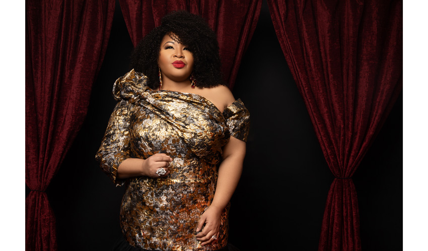 Photograph of female singer in gold dress against backdrop of crushed red velvet curtains