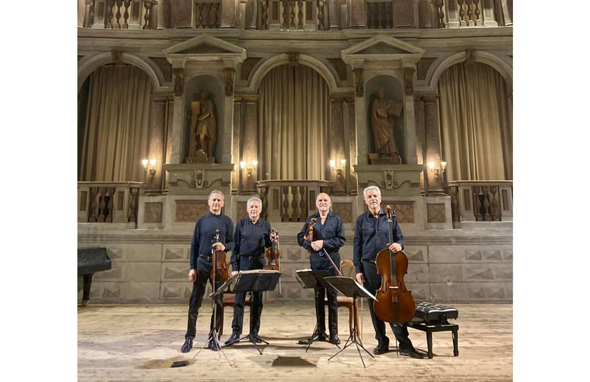 photo of four standing musicians in black holding their string instruments against an ornate background interior