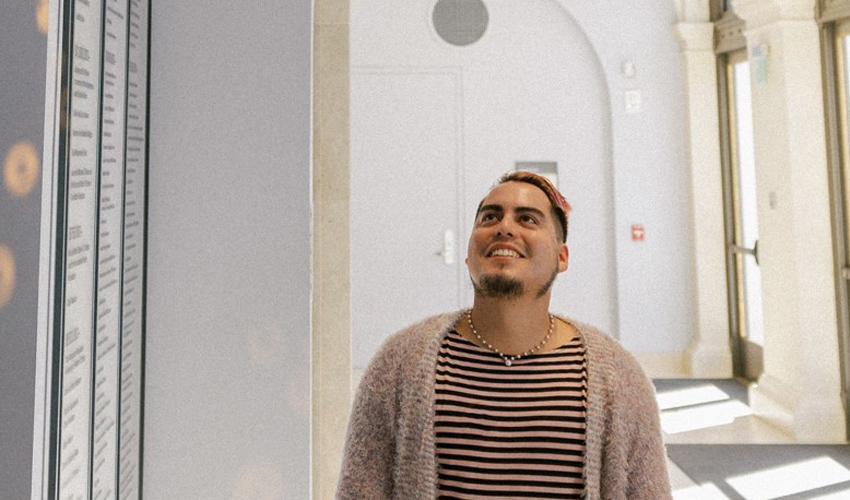 interior photo of person in a stripe shirt and cardigan sweater facing camera and looking up towards the ceiling