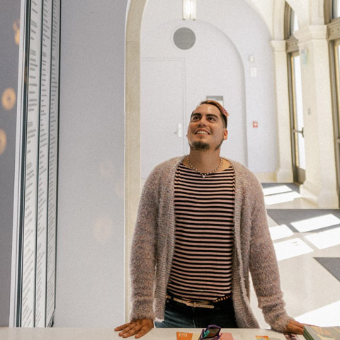 interior photo of person in a stripe shirt and cardigan sweater facing camera and looking up towards the ceiling