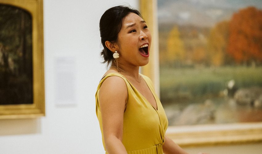 photo of a singer in a yellow dress performing in front of a painting