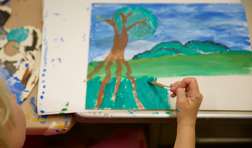 photo of child painting a landscape