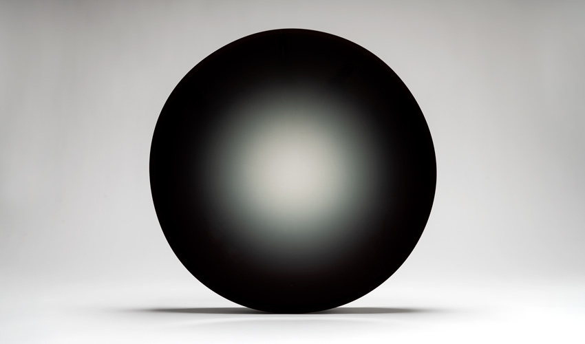 photo of dark and round work of art with a seemingly flat and shiny surface against a light gray backdrop