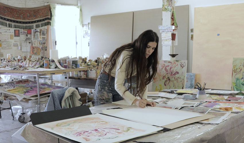 photo of the artist working in her studio, bent over a table drawing