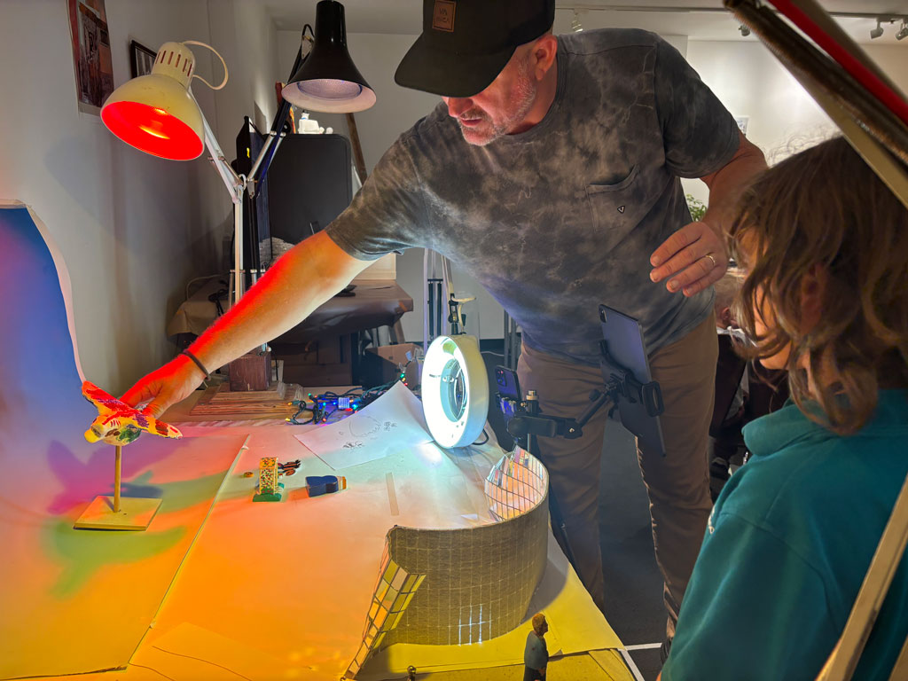 photo of a teacher with a hat on instructing kid on film technique and moving item being filmed