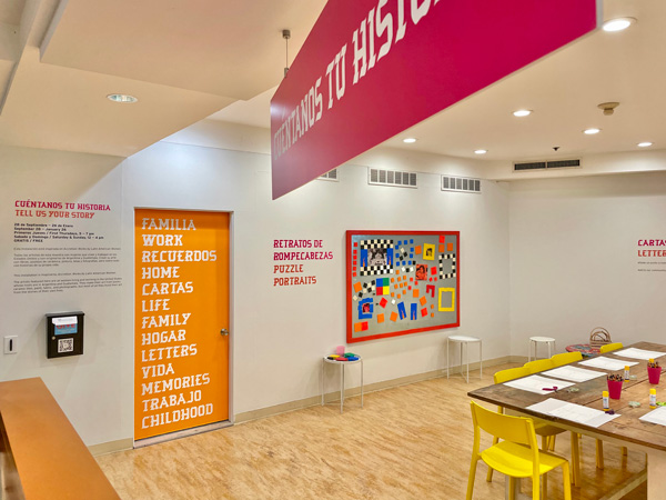 photo of interior of learning center featuring various text and decoration including orange door with words in english and spanish, a work table, and cork board for crafts