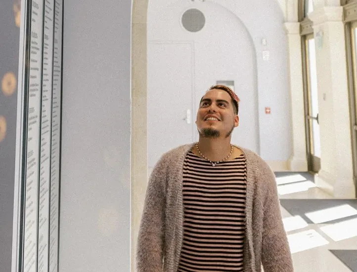 interior photo of person in a stripe shirt and cardigan sweater facing camera and looking up towards the ceiling