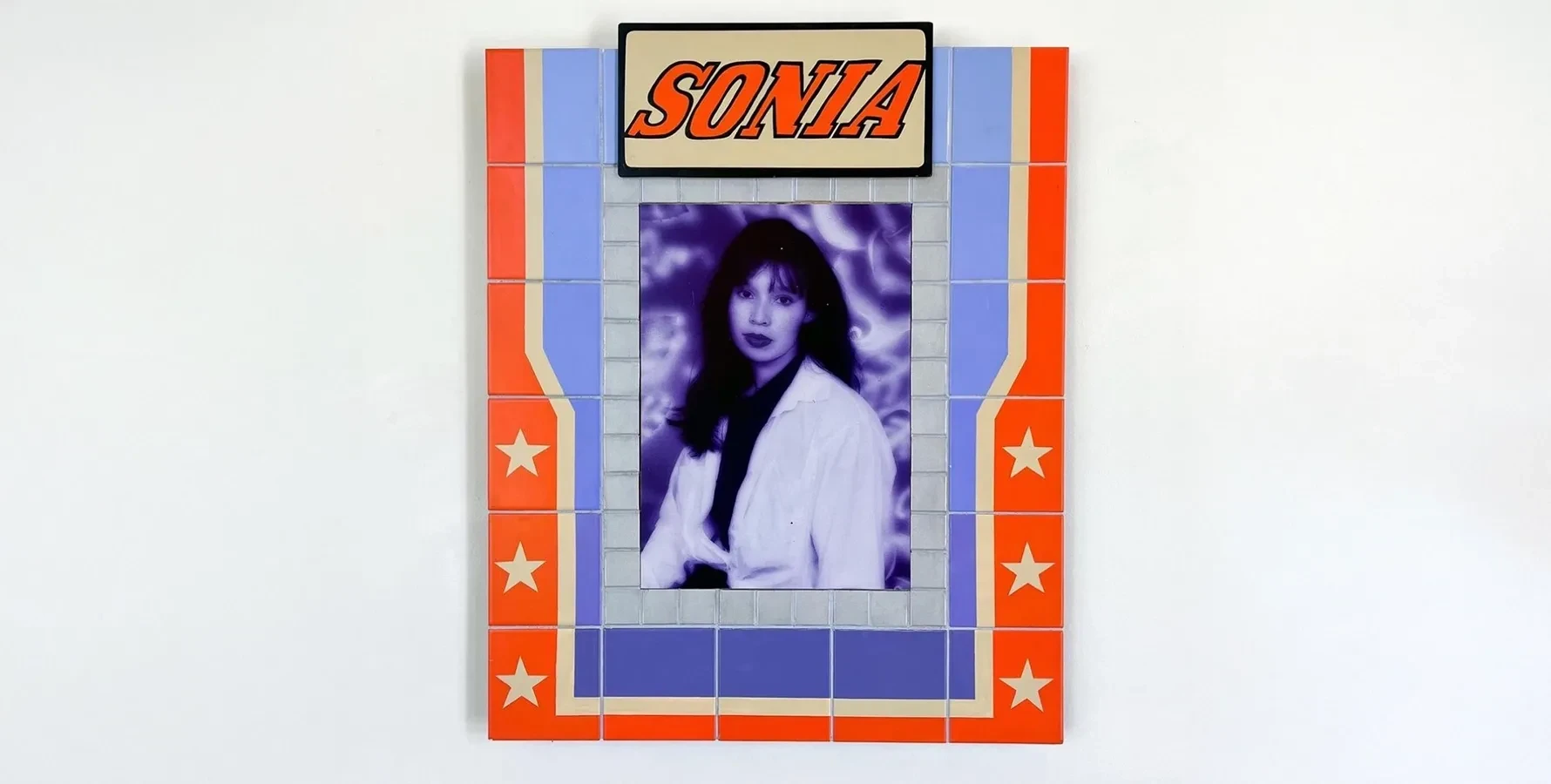 flat sculpture featuring a monochrome blue and purple portrait in the center surrounded by orange titles and the word Sonia at the top