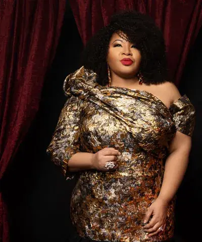 Photograph of female singer in gold dress against backdrop of crushed red velvet curtains