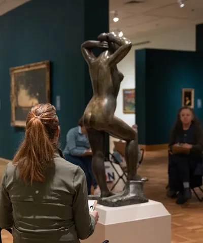 photo of patrons in a gallery interior drawing from a sculpture of a figure