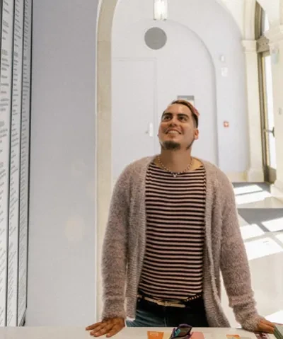 interior photo of person in a stripe shirt and cardigan sweater facing camera and looking up towards the ceiling