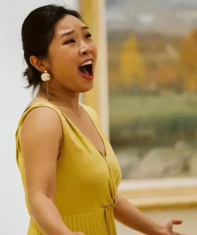 photo of a singer in a yellow dress performing in front of a painting