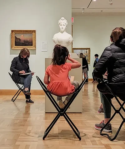 visitors of all ages sketching a plaster bust in a museum gallery