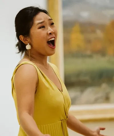 photo of a singer in a yellow dress performing in front of a painting