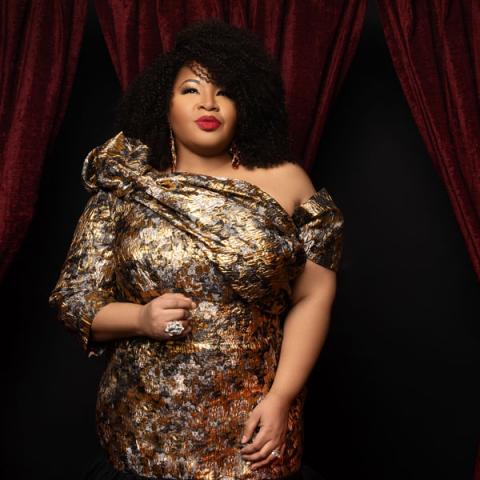 Photograph of female singer in gold dress against backdrop of crushed red velvet curtains