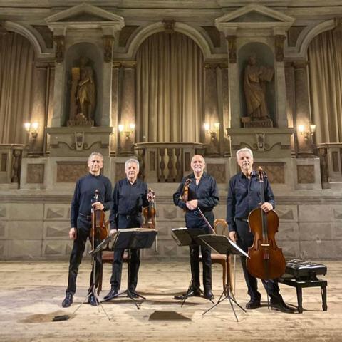 photo of four standing musicians in black holding their string instruments against an ornate background interior