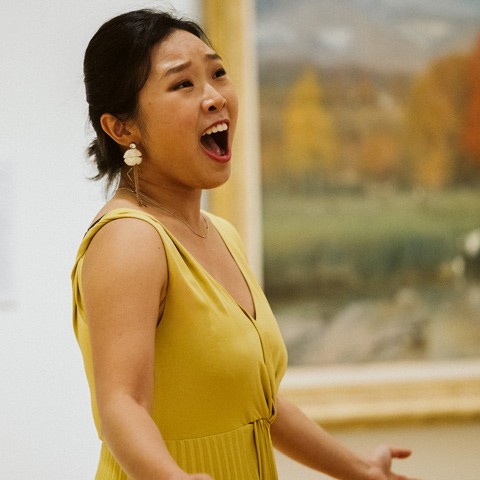 photo of a singer in a yellow dress performing in front of a painting