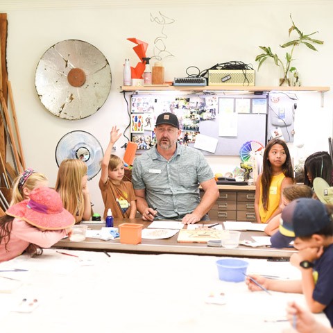 photo of an instructor in baseball camp leading children in arts and crafts projects at a table