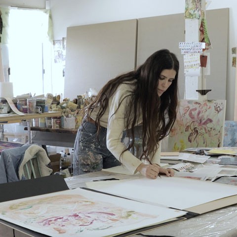 photo of the artist working in her studio, bent over a table drawing