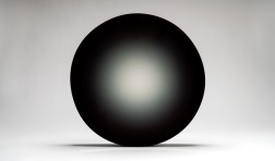 photo of dark and round work of art with a seemingly flat and shiny surface against a light gray backdrop