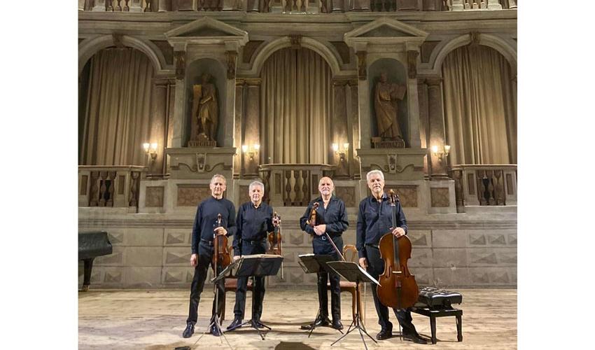 photo of four standing musicians in black holding their string instruments against an ornate background interior